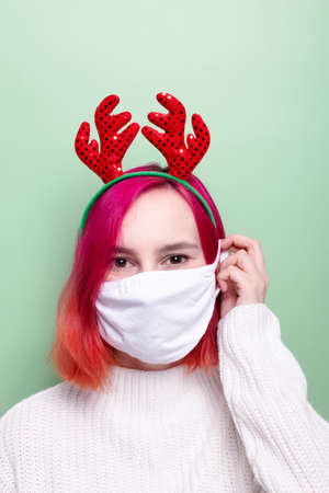 Woman in white sweater and deer horns, puts on white mask, green backgroundの写真素材