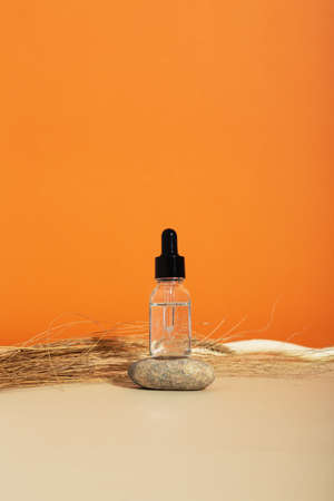 Bottle white glass with dropper on orange background. Natural cosmetic product for skincare concept. Natural materials, rock balancingの写真素材