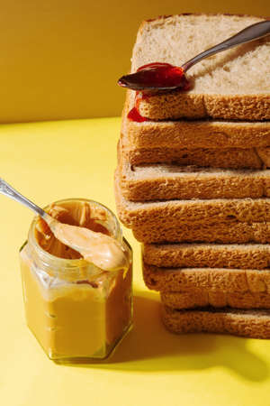 Ingredients for peanut butter and jelly sandwiches. Spoon with strawberry jam on pile of toast breadの写真素材