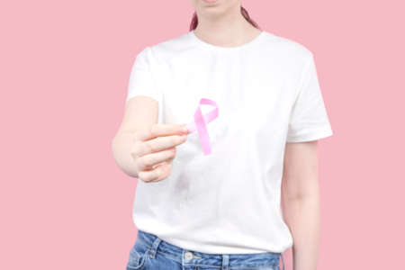 World Breast cancer day concept. Woman in white T-shirt holds pink ribbon in hand. October Breast...
