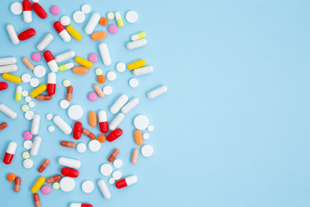 Various white medication tablets and capsules on blue background. Concept of healthcare and...