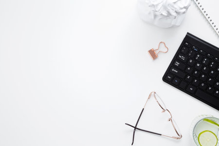 Workplace with white notebook, black keyboard, stationery, glass of water with lime and glasses on white desk. Flat lay office desk, mock up space for text. top view. copy spaceの写真素材