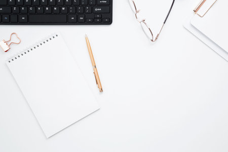 Workplace with white notebook, black keyboard, stationery, glass of water with lime and glasses on white desk. Flat lay office desk, mock up space for text. top view. copy spaceの写真素材