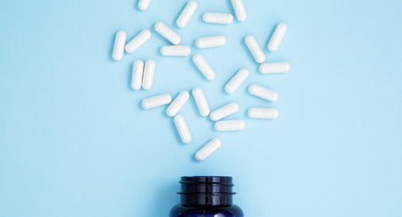 Blue bottle container with white medication capsules on blue background. Concept of healthcare and...