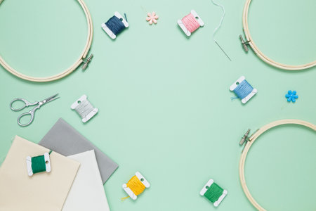 Embroidery set fot stitching on green background with embroidery hoop, fabric, colorful threads, scissors and needls. Indoor hobby concept with copy space, top viewの写真素材