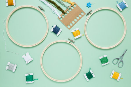 Embroidery set fot stitching on green background with embroidery hoop, fabric, colorful threads, scissors and needls. Indoor hobby concept with copy space, top viewの写真素材