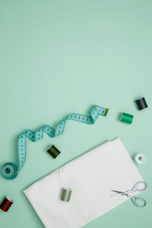 Composition with various threads and sewing accessories on green background. Top view, copy space