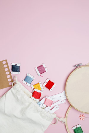Embroidery set fot stitching. Beige cotton cloth in embroidery hoop on pink background with fabric, colorful threads, scissors and needslsの写真素材
