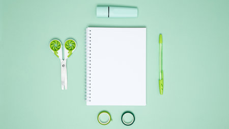 Creative flat lay mockup design of workspace. Top view composition with white notebook, to do list and stationery on green backgroundの写真素材