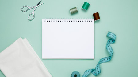 Composition with various threads and sewing accessories on green background. Mock up notebook
