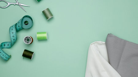 Composition with various threads and sewing accessories on green background. Top view, copy space