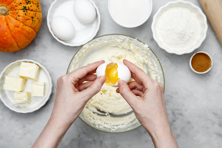 Ingredients for autumn baking. Woman breaks an egg into a bowl of dough