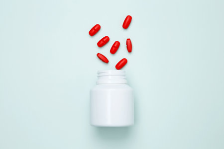 Bottles with red pills scattered on a light blue background. Concept of medicine, healthcare, and pharmaceutical industryの写真素材