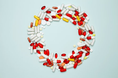 Various colorful pills and capsules scattered on a light blue background. Concept of medicine, healthcare, and pharmaceutical industryの写真素材