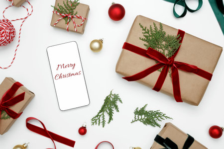 Wrapped Christmas gifts with tuja sprigs and smartphone displaying "Merry Christmas" messageの写真素材