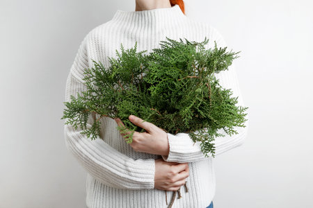 A woman in a white sweater holding thuja branches, symbolizing winter and natural beautyの写真素材