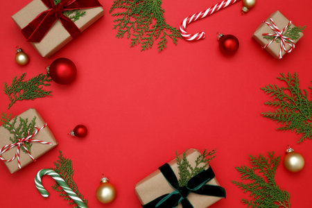 Gifts wrapped in craft paper, Christmas ornaments, thuja branches, and candy cane arranged on red backgroundの写真素材
