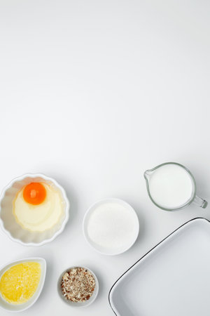 Flat lay composition for cooking preparation. Empty white baking dish with ingredients for baking, including egg, milk, butter, sugar, nutsの写真素材