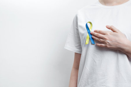 A person wearing a white t-shirt with a yellow and blue awareness ribbon, symbolizing World Down Syndrome Dayの写真素材