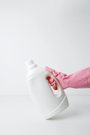 Female hand in a pink rubber glove holding a white mockup of laundry gel packaging. Household cleaning and hygiene concept packagingの写真素材