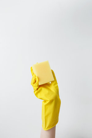 Hand in yellow rubber glove holding a sponge for cleaning. Household cleaning and hygiene concept conceptの写真素材