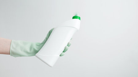 Household cleaning and hygiene concept. Hand in rubber glove holding cleaning product bottle during houseworkの写真素材