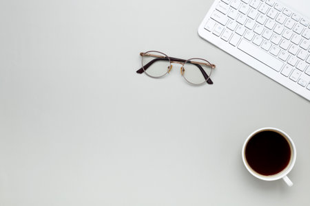 Cozy workspace with coffee cup, keyboard, glasses creating focused morning atmosphereの写真素材