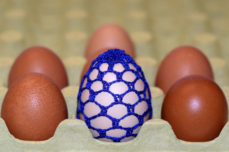 Blue egg with crocheting among other eggs in a container