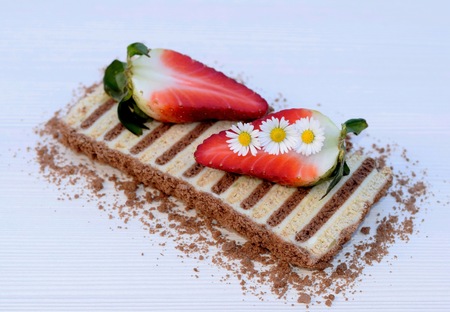 Unbaked layered dessert made of flat biscuits and curd, decorated with daisies and strawberriesの写真素材