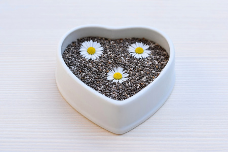 Chia seeds (Salvia hispanica) in a ceramic bowl of heart shape, decorated with flowersの写真素材