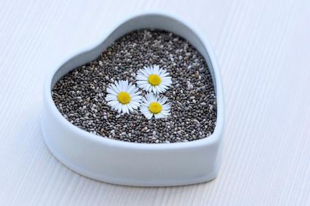 Chia seeds (Salvia hispanica) in a ceramic bowl of heart shape, decorated with flowersの写真素材