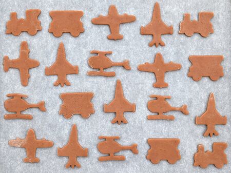 Cut gingerbreads in a shape of airplane, helicopter and train on a baking tray ready for bakingの写真素材
