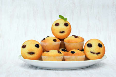 Freshly baked homemade muffins, some with funny faces. Vanilla muffins with raisins, decorated with...