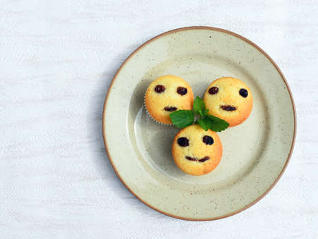 Freshly baked homemade muffins with funny faces. Vanilla muffins with raisins, decorated with melissa leafsの写真素材