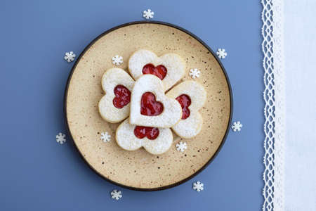 Heart shaped linzer cookies filled with strawberry jam, decorative small sugar snowflakes around....