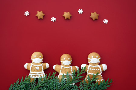 Cute gingerbread family with protective face masks on red background with decoration. Creative...
