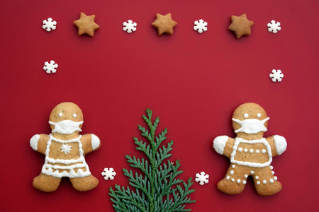 Cute gingerbread couple with protective face masks on red background with decoration. Creative concept in coronavirus (COVID-19) time. Christmas or New year greeting card, copy space for textの写真素材