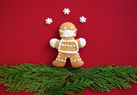 Cute gingerbread man with protective face mask on red background with decoration. Creative concept in coronavirus (COVID-19) time. Christmas or New year greeting card, copy space for textの写真素材