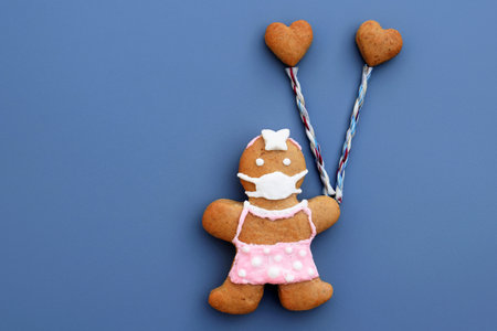 Cute gingerbread woman with protective face mask and hearts on blue background. Original love...