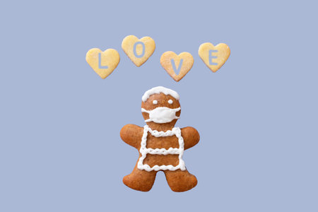 Cute gingerbread man with protective face mask and hearts with inscription LOVE isolated on pastel...