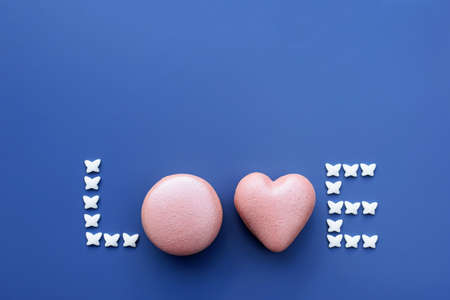 Word LOVE made of pink heart and round shape macarons and small butterflies. Sweets, love concept, greeting card, copy space for textの写真素材