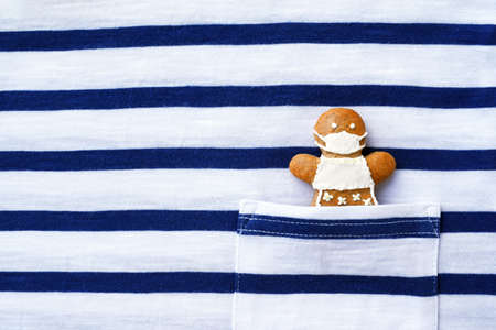 Cute gingerbread woman with protective face mask in the pocket of a striped t-shirt. Creative conceptの写真素材