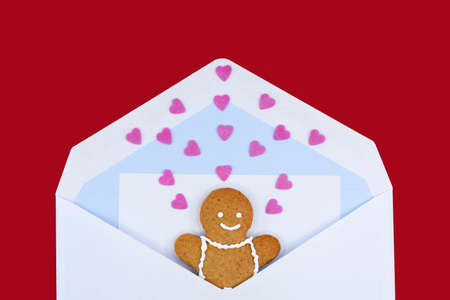 Smiling gingerbread man in an envelope with a letter and many sweet hearts, red background. The concept of love, greeting card for Valentine's Day, Mother's Day or birthdayの写真素材