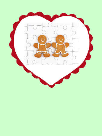 Heart with smiling gingerbread man and woman on completed white jigsaw puzzle, isolated on green...