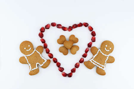 Smiling gingerbread man, woman and small hearts in big red heart made of pomegranate seeds. The...