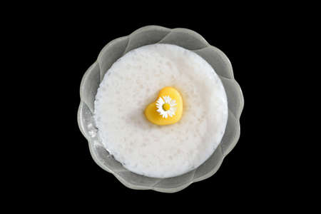 Homemade tapioca pudding with coconut milk, decorated with fresh nectarine in a shape of heart and edible daisy flower. Isolated on black background. Romantic concept, inspirationの写真素材