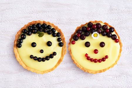 Smiling fruit cakes. Shortbread tartlets with vanilla custard cream, black and red currant and fruits of amelanchier. Creative bakingの写真素材