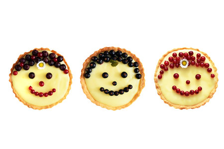 Smiling fruit cakes. Shortbread tartlets with vanilla custard cream, black and red currant and fruits of amelanchier. Isolated, top view. Creative bakingの写真素材