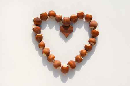 Heart made of hazelnuts in shell and wooden heart, white backgroundの写真素材