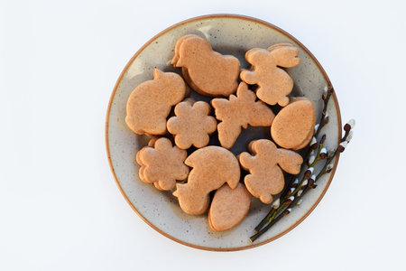Undecorated Easter gingerbread cookies of various shapes on a plate with willow twigs, white...